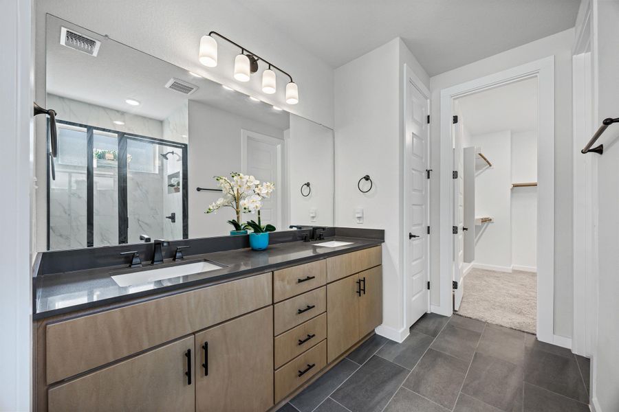 Primary bath featuring a marble finish shower, double vanity, stone countertops, and dark tile patterned floors