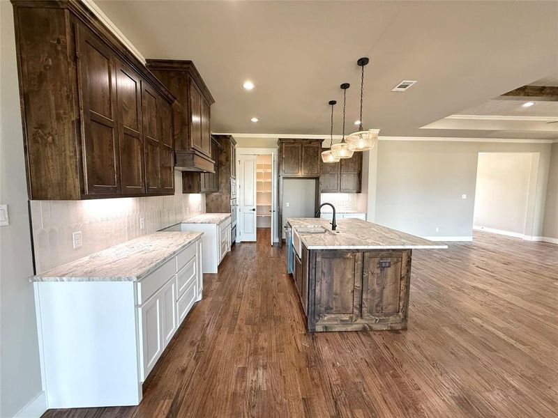 Kitchen featuring decorative backsplash, dark brown cabinets, light stone counters, hanging light fixtures, and dark wood-style flooring Kitchen featuring decorative backsplash, dark brown cabinets, light stone counters, hanging light fixtures, and dark wood-style flooring