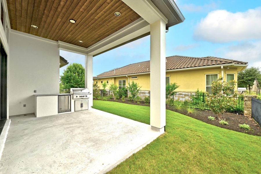 Covered outdoor patio featuring a wood-finish ceiling with recessed lighting, an integrated grill station with stainless steel appliances, and a concrete patio floor