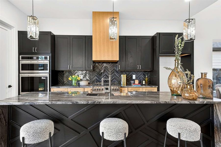 Kitchen featuring a breakfast bar, dark stone counters, hanging light fixtures, and dark cabinets Kitchen featuring a breakfast bar, dark stone counters, hanging light fixtures, and dark cabinets