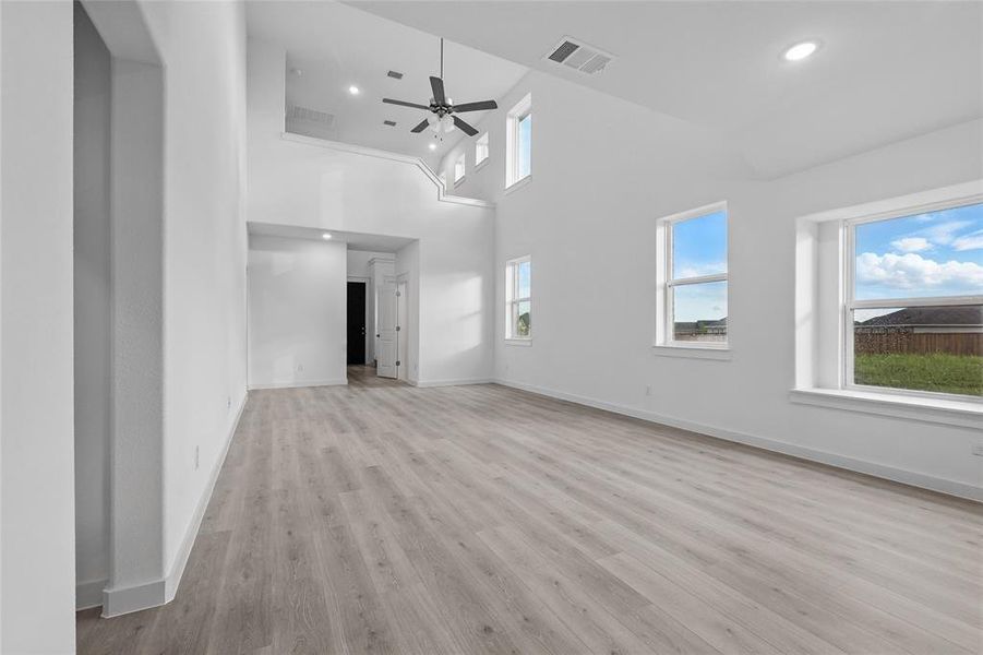 Empty room with a towering ceiling, light wood-style flooring, ceiling fan, and recessed lighting