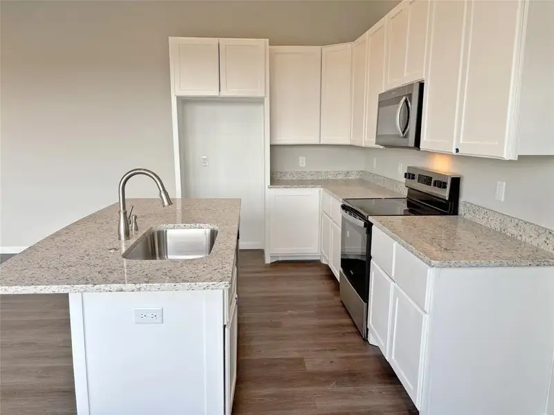 Kitchen with stainless steel appliances, a kitchen island with sink, dark wood finished floors, white cabinets, and light stone counters