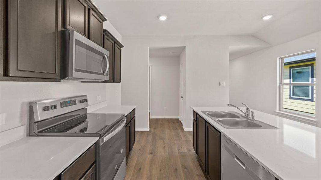 Kitchen featuring dark wood cabinetry, stainless steel appliances, light countertops, wood-finish flooring, and recessed lighting