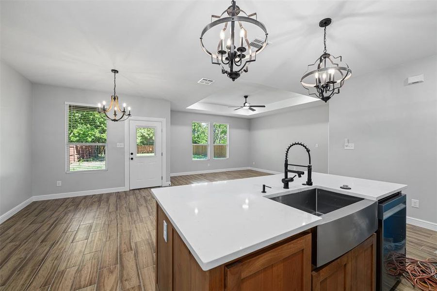 Kitchen featuring a center island with sink, ceiling fan with notable chandelier, dark hardwood / wood-style flooring, and decorative light fixtures