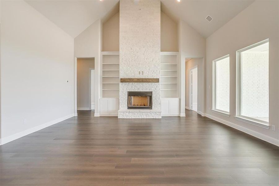 Unfurnished living room with dark hardwood / wood-style floors, built in shelves, a fireplace, and high vaulted ceiling