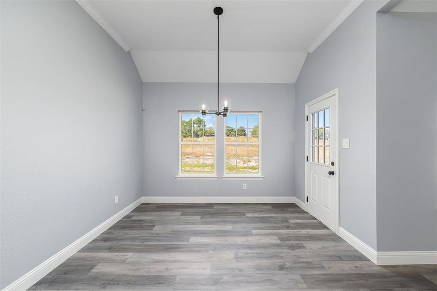 Unfurnished dining area with ornamental molding, a chandelier, wood finished floors, and lofted ceiling Unfurnished dining area with ornamental molding, a chandelier, wood finished floors, and lofted ceiling