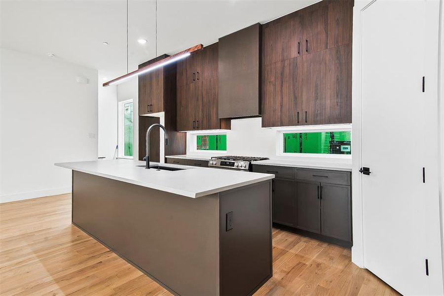 Kitchen with stainless steel gas range oven, a kitchen island with sink, sink, light hardwood  flooring, and dark brown cabinets