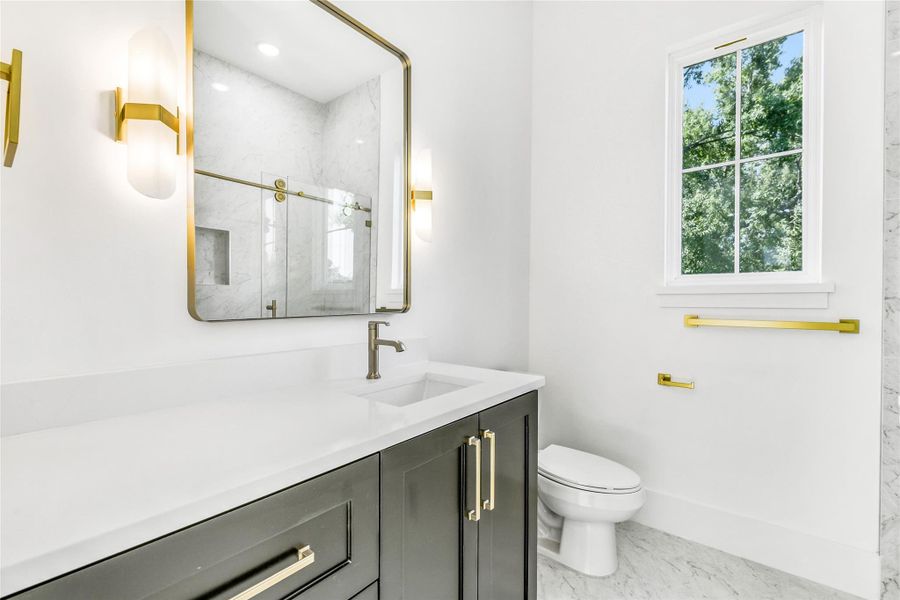 The ensuite bathroom continues the home’s luxury aesthetic with quartz countertops, black shaker cabinetry, and brushed brass hardware and lighting. The frameless glass shower enclosure is fully tiled in marble-pattern porcelain, featuring a brass sliding door system, recessed shampoo niche, and designer fixtures. Every element blends craftsmanship with timeless design for a spa-quality experience in a private setting.