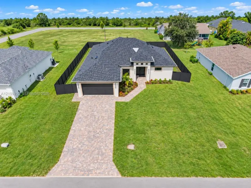 Single-story residence featuring a dark shingle roof, a paved paver driveway, and an enclosed backyard with black metal fencing