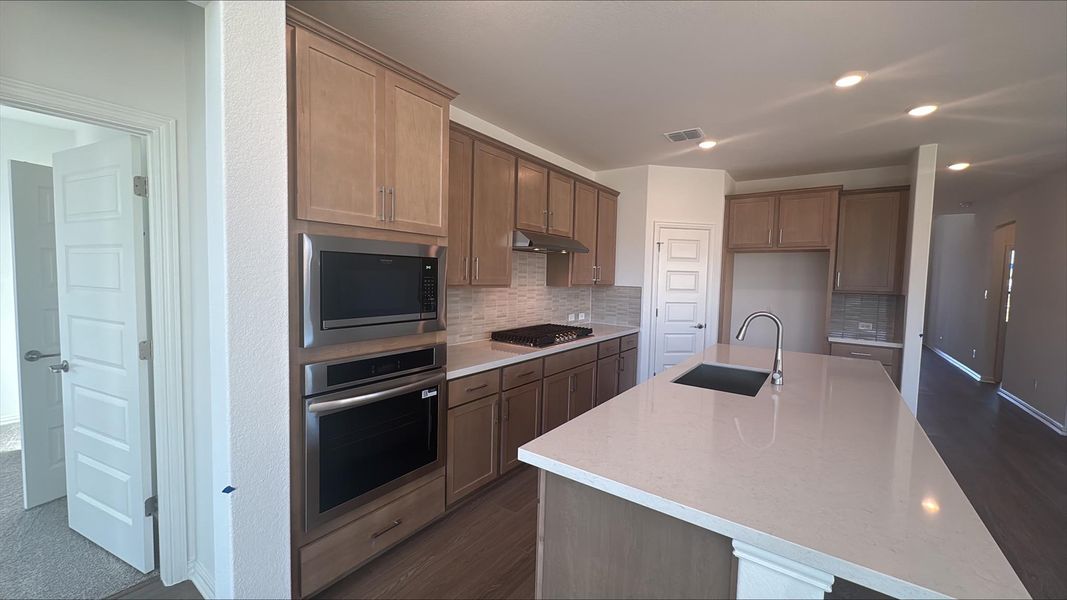Kitchen with appliances with stainless steel finishes, light stone countertops, backsplash, a kitchen island with sink, and dark wood finished floors