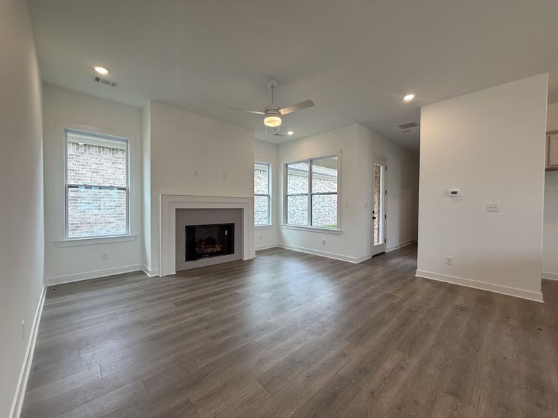 Spacious living area featuring light wood-finish flooring, a white mantel fireplace with a dark gray surround, and recessed lighting