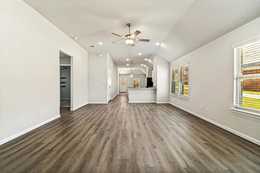 Spacious living area featuring wood-finish flooring, vaulted ceilings, and recessed lighting Spacious living area featuring wood-finish flooring, vaulted ceilings, and recessed lighting