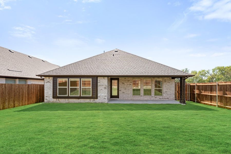 Rear view of single-story brick home with covered patio, large windows, and fenced backyard with green lawn.