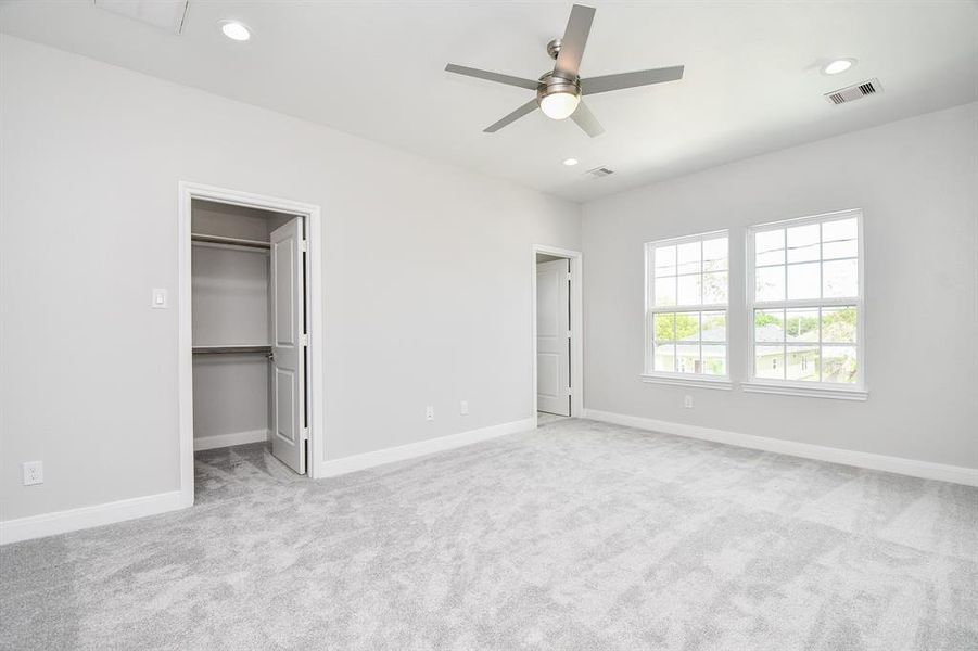 This is a bright, spacious Primary room with plush carpeting, featuring a ceiling fan, two large windows for natural light, and a built-in closet for storage.