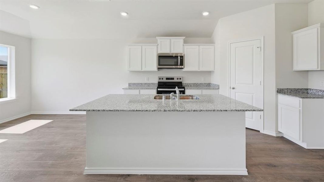 Kitchen with light stone countertops, white cabinetry, an island with sink, stainless steel appliances, and recessed lighting