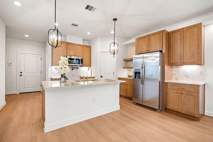 Stylish open kitchen featuring warm wood cabinetry, quartz countertops, and a large center island with seating. Stainless steel appliances, designer pendant lighting, and a sleek tile backsplash complete this bright and functional space, perfect for cooking and entertaining.