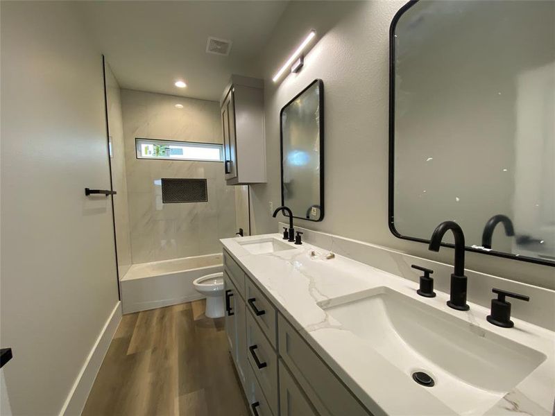 Full bathroom with wood-type flooring, toilet, tiled shower / bath, and vanity