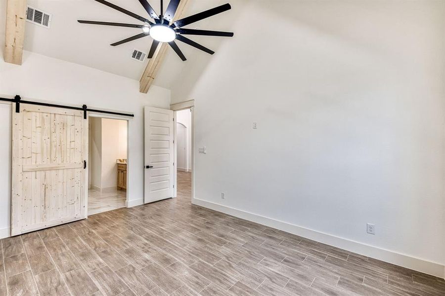 Unfurnished bedroom featuring a barn door, wood finish floors, ensuite bath, lofted ceiling, and ceiling fan