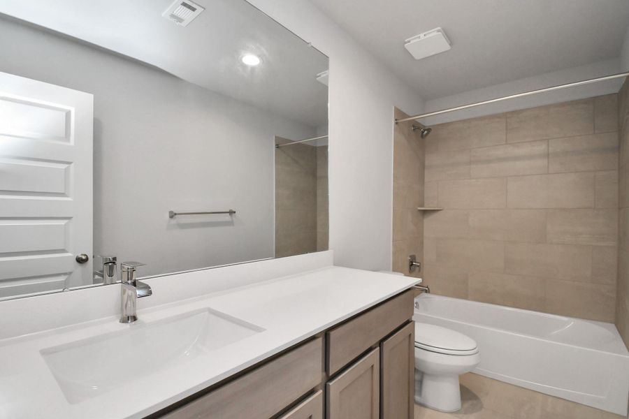 Secondary bath features tile flooring, bath/shower combo with tile surround, light stained wood cabinets, beautiful light countertop. Sample photo of completed home with similar floor plan. Actual colors and selections may vary.