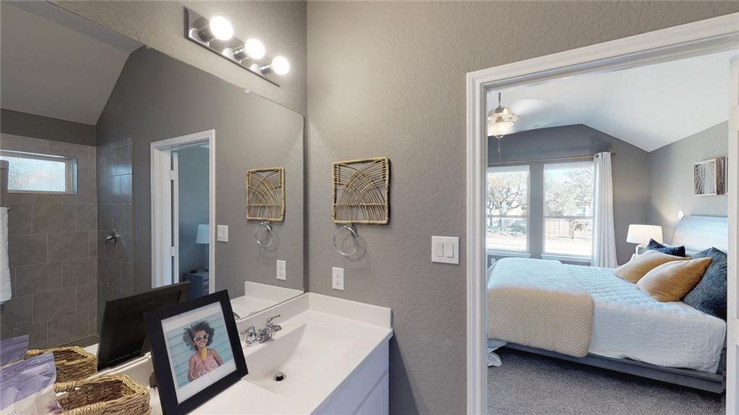 Ensuite bathroom featuring vaulted ceiling, a textured wall, vanity, and tiled shower Ensuite bathroom featuring vaulted ceiling, a textured wall, vanity, and tiled shower