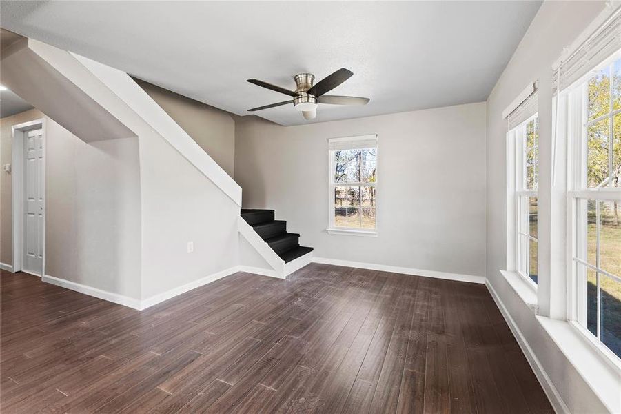 Unfurnished living room with dark wood-style flooring, stairs, and a ceiling fan