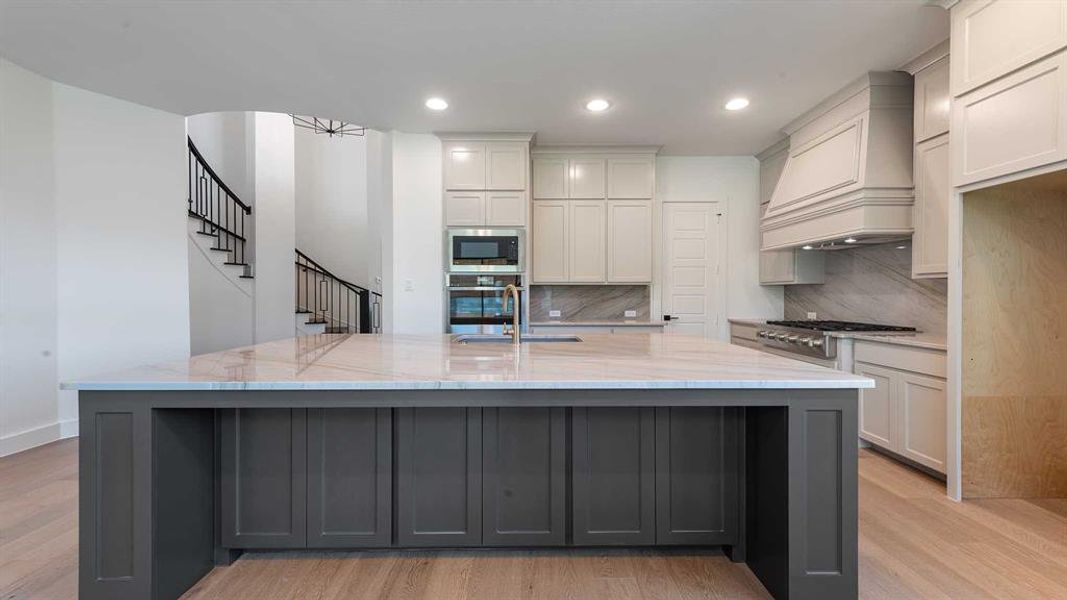 Kitchen with stainless steel appliances, premium range hood, light wood-style floors, decorative backsplash, and recessed lighting