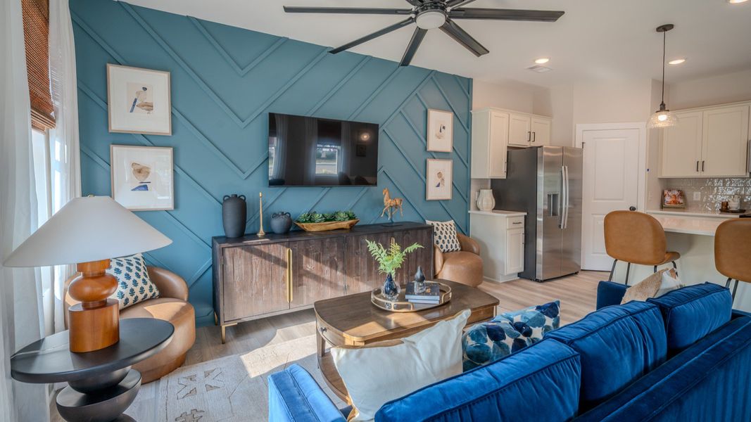 Living area with ceiling fan, accent wall, and access to kitchen