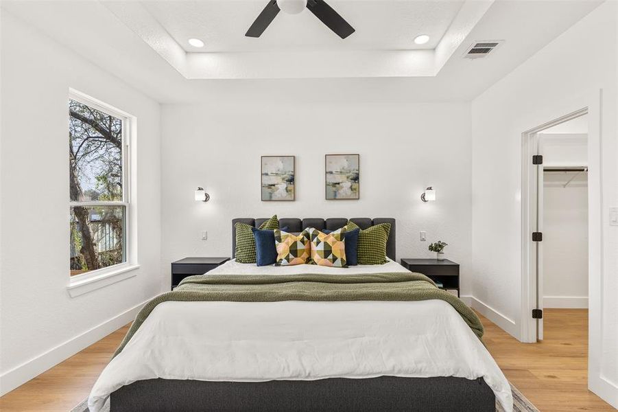 Bedroom with a raised ceiling, light wood-type flooring, ceiling fan, recessed lighting, and a walk in closet