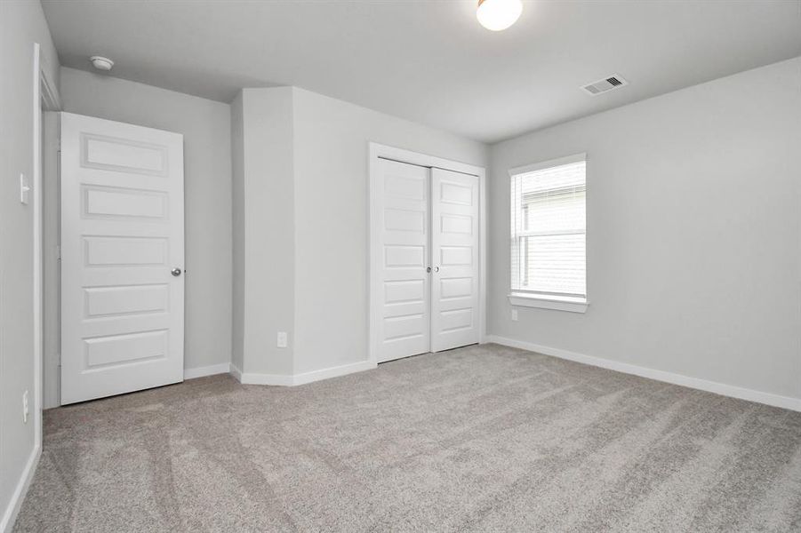 Secondary bedroom features plush carpeting, large windows that let in plenty of natural light, bright paint, and spacious closets.