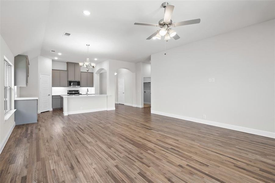 Unfurnished living room featuring dark wood-style floors, a chandelier, arched walkways, recessed lighting, and a ceiling fan