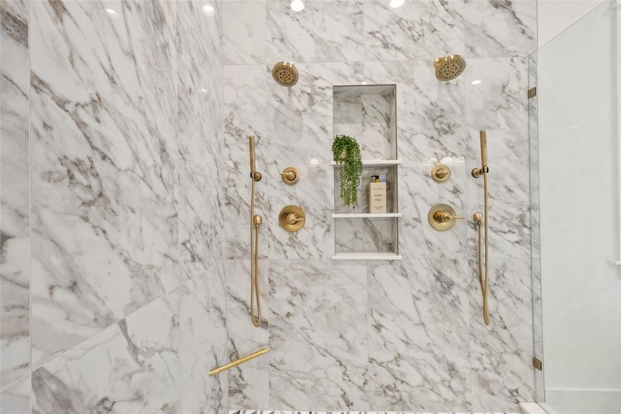 You step into a true spa experience with floor-to-ceiling marble, dual shower heads, handheld fixtures, and a built-in niche for everyday essentials. The symmetry, warm brass finishes, and oversized layout turn your daily routine into a moment of luxury.