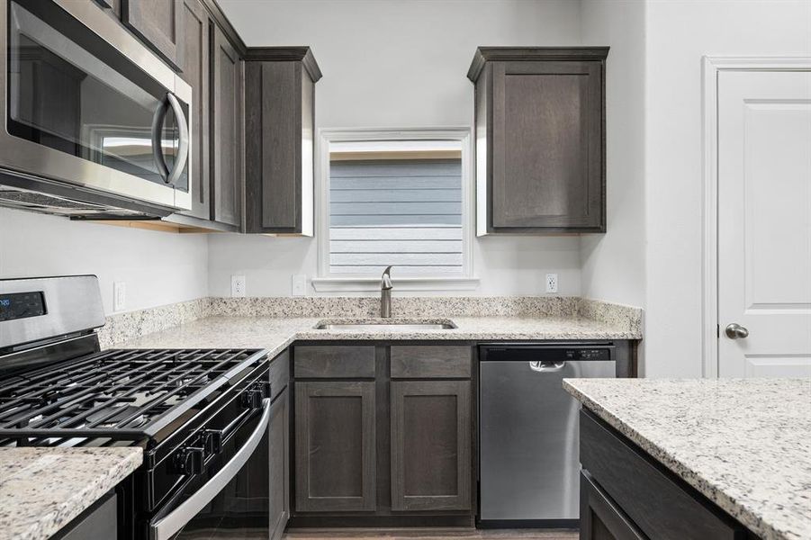 Kitchen with appliances with stainless steel finishes, light stone counters, dark brown cabinetry, and light wood-type flooring