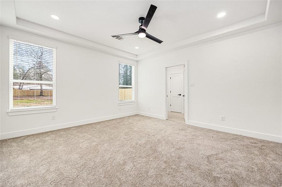 Primary Bedroom-This bright, spacious bedroom features plush carpeting, recessed lighting, and a modern ceiling fan. Large windows provide ample natural light, and a doorway leads to an adjoining room or closet.