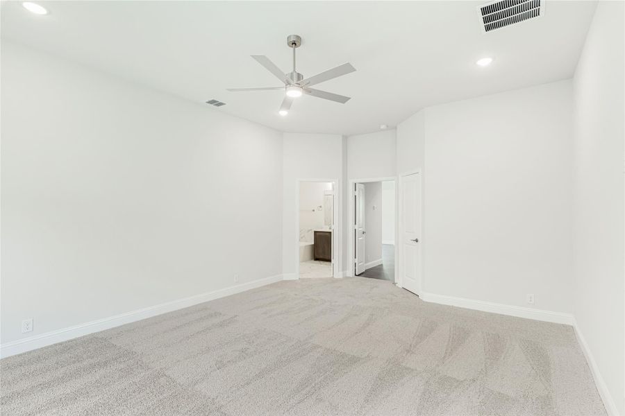 Empty bedroom with gray carpet, ceiling fan, and open door to ensuite bathroom Empty bedroom with gray carpet, ceiling fan, and open door to ensuite bathroom