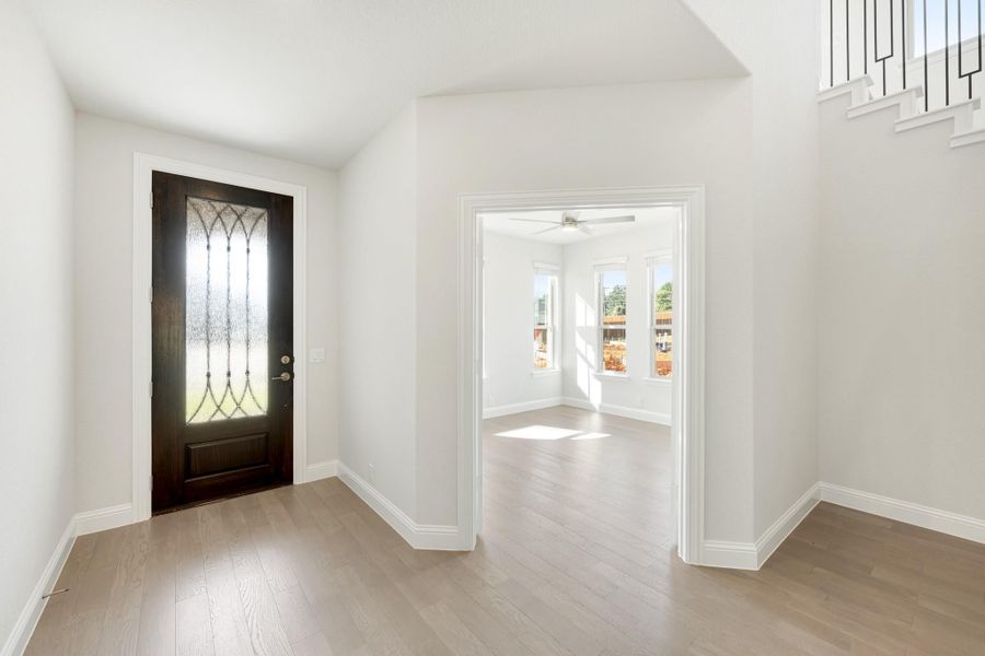 Entryway with dark wood front door featuring decorative glass panel and light hardwood floors leading to an adjacent room