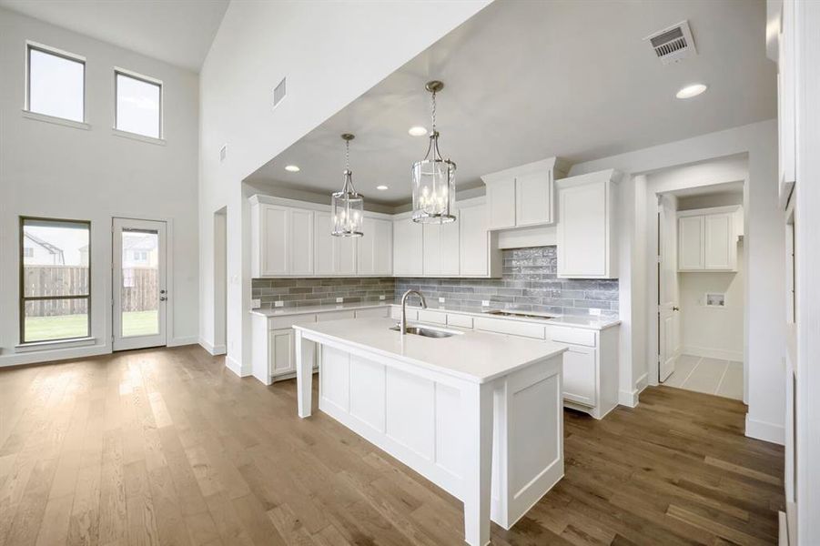 Contemporary kitchen featuring white cabinetry, a large center island with a sink, quartz-finish countertops, and a gray subway tile backsplash Contemporary kitchen featuring white cabinetry, a large center island with a sink, quartz-finish countertops, and a gray subway tile backsplash