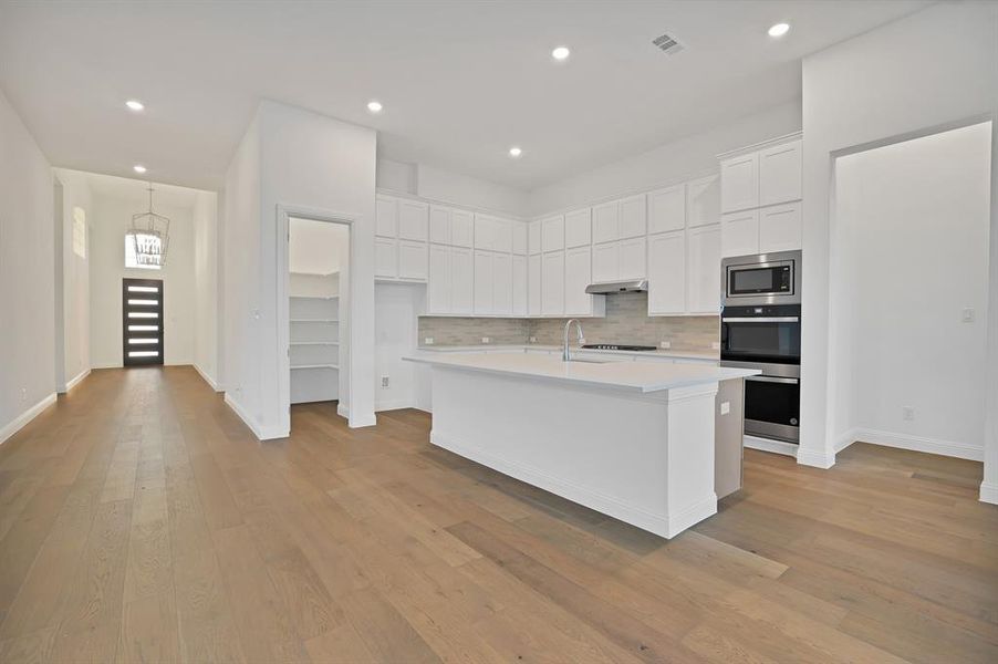 Kitchen featuring tasteful backsplash, a kitchen island with sink, white cabinetry, and appliances with stainless steel finishes