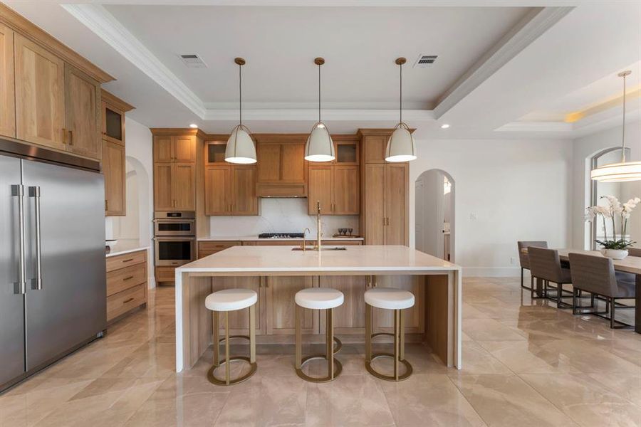 Amble storage space, elegant pendant lighting, and a dining area to the side. The room features high ceilings with crown molding and a bright, airy feel thanks to ample natural light.