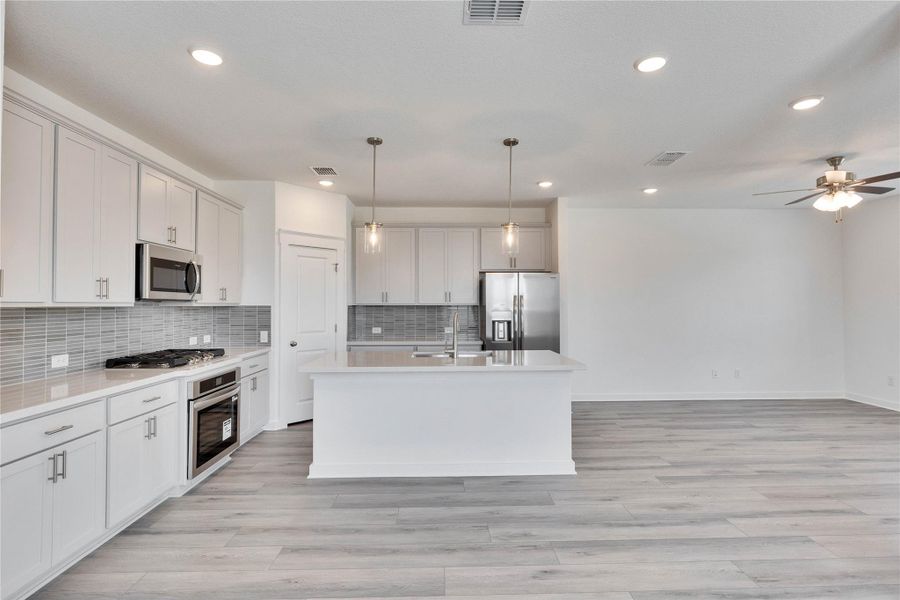 Kitchen featuring a center island with sink, hanging light fixtures, stainless steel appliances, recessed lighting, and decorative backsplash