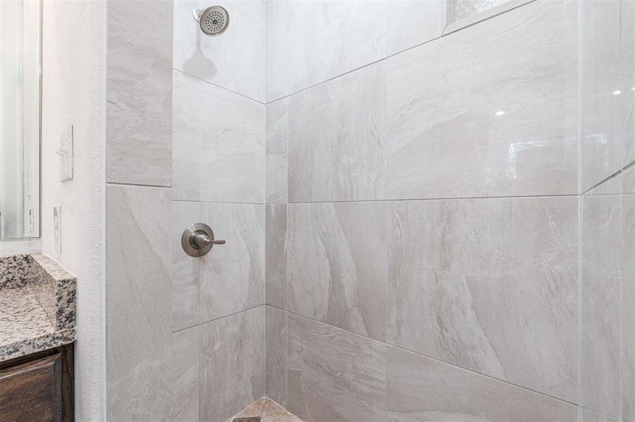 Bathroom featuring tiled shower and vanity