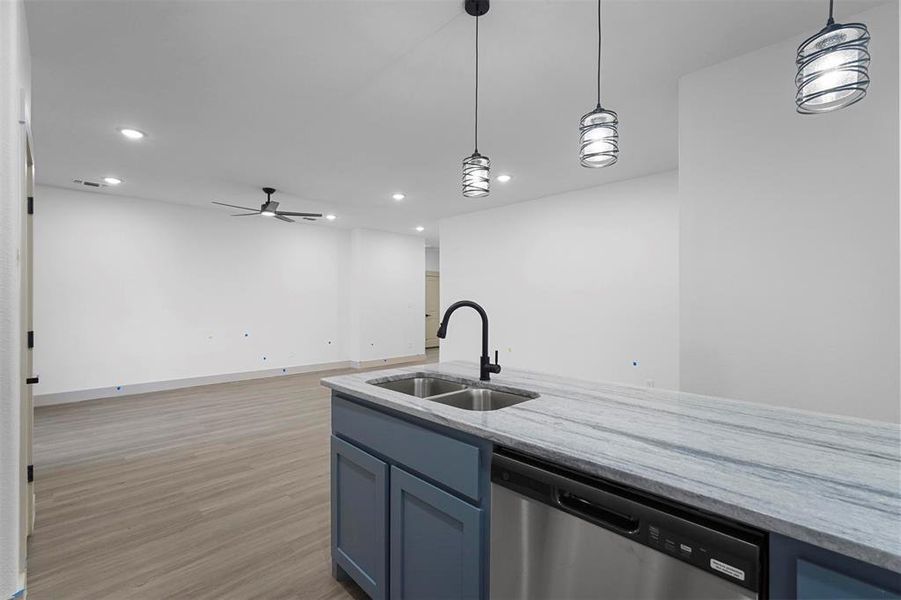 Kitchen with a sink, light wood-type flooring, light stone counters, and stainless steel dishwasher