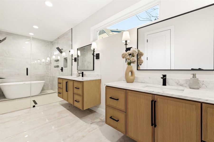 Full bathroom featuring two vanities, a stall shower, a freestanding bath, and recessed lighting
