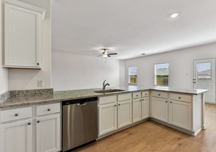 Kitchen featuring a granite peninsula, stainless dishwasher, white cabinetry, and a ceiling fan beyond.