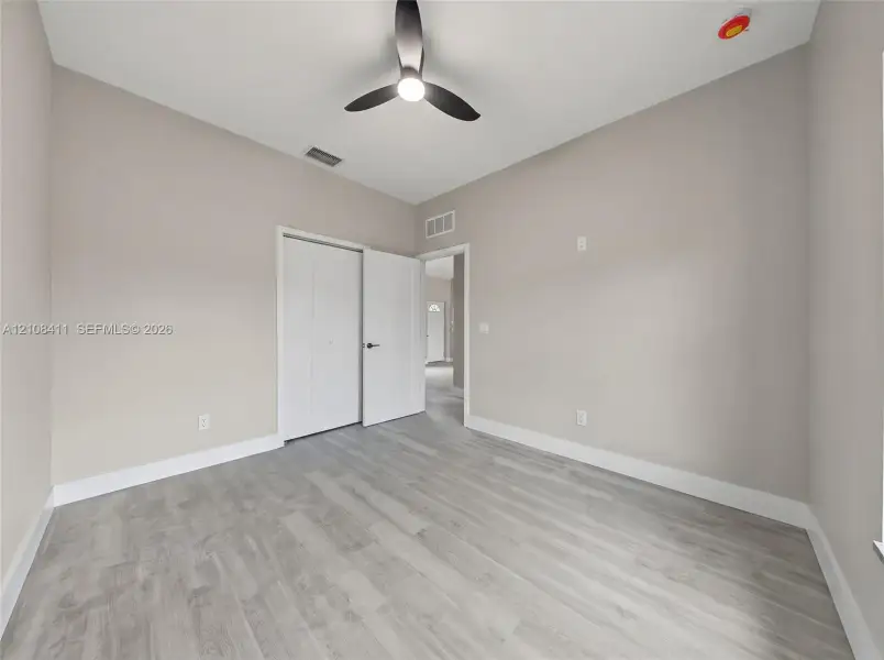 Neutral-toned interior featuring wood-finish flooring, a modern three-blade ceiling fan with integrated lighting, and a dual-panel closet door