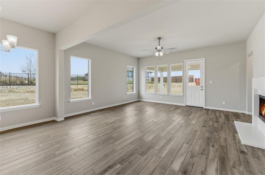 Unfurnished living room with a warm lit fireplace, a ceiling fan, and light wood finished floors