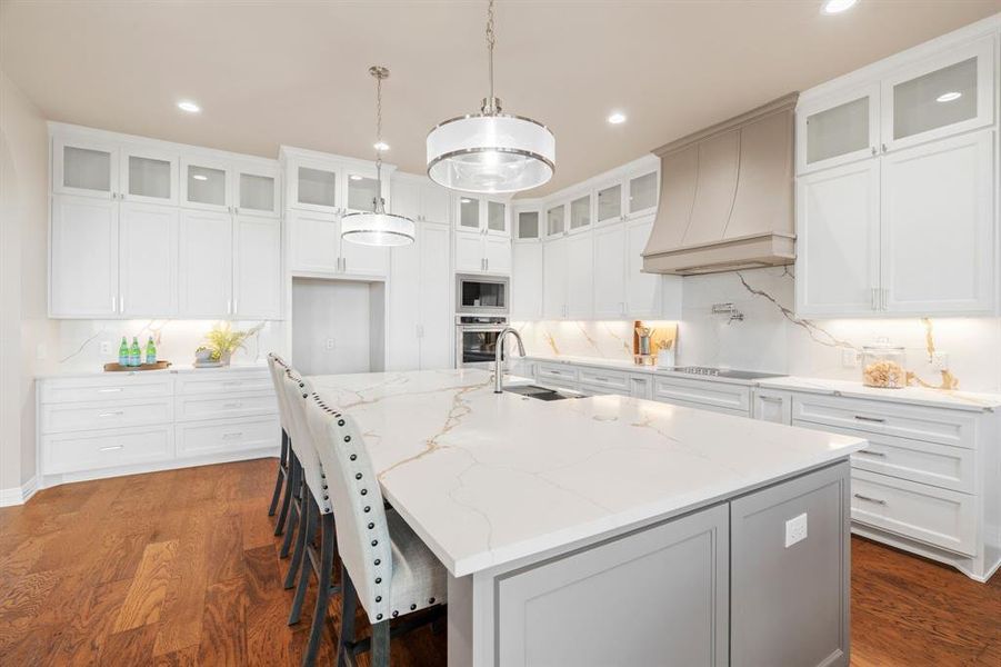 Kitchen featuring oven, white cabinetry, custom range hood, an island with sink, and built in microwave