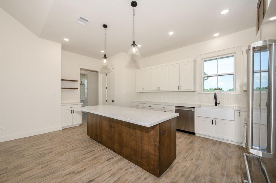 Kitchen featuring white cabinets, stainless steel appliances, a kitchen island, decorative backsplash, and recessed lighting
