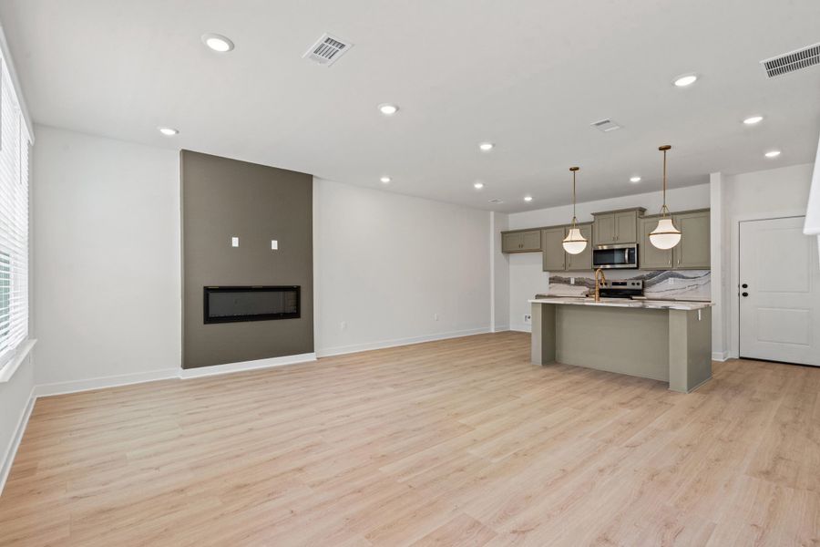 Spacious open-concept living area featuring wood-finish flooring, recessed lighting, and an electric fireplace