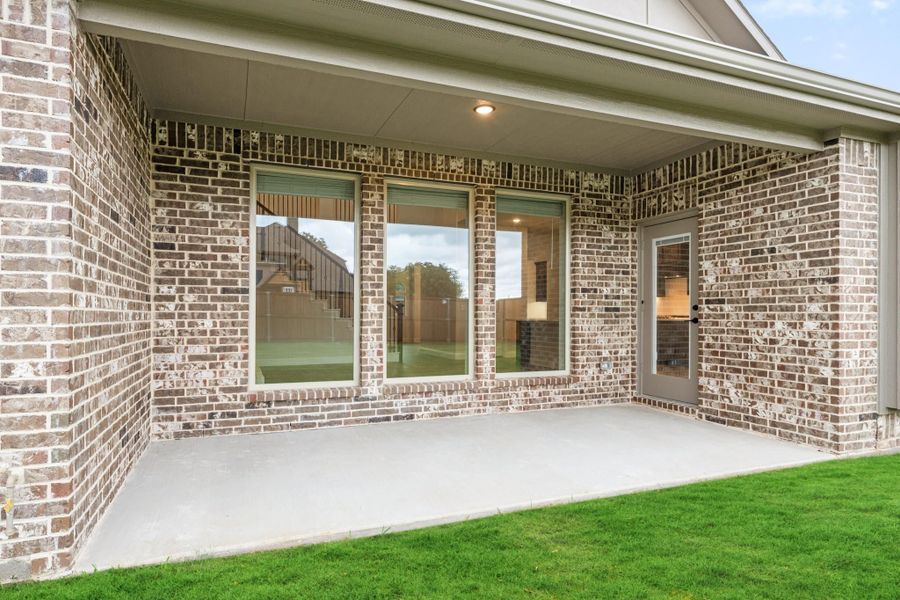 Covered back patio with concrete floor, brick exterior, large windows, and glass door overlooking green lawn Covered back patio with concrete floor, brick exterior, large windows, and glass door overlooking green lawn