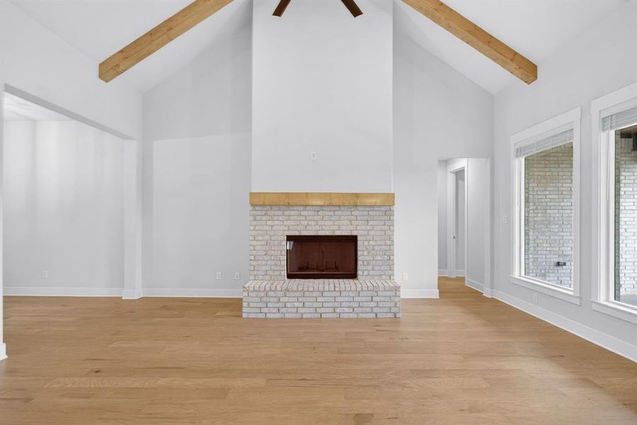 Vaulted ceiling with exposed wood beams, a white brick fireplace with a wood mantle, light wood-finish flooring, and multiple windows Vaulted ceiling with exposed wood beams, a white brick fireplace with a wood mantle, light wood-finish flooring, and multiple windows